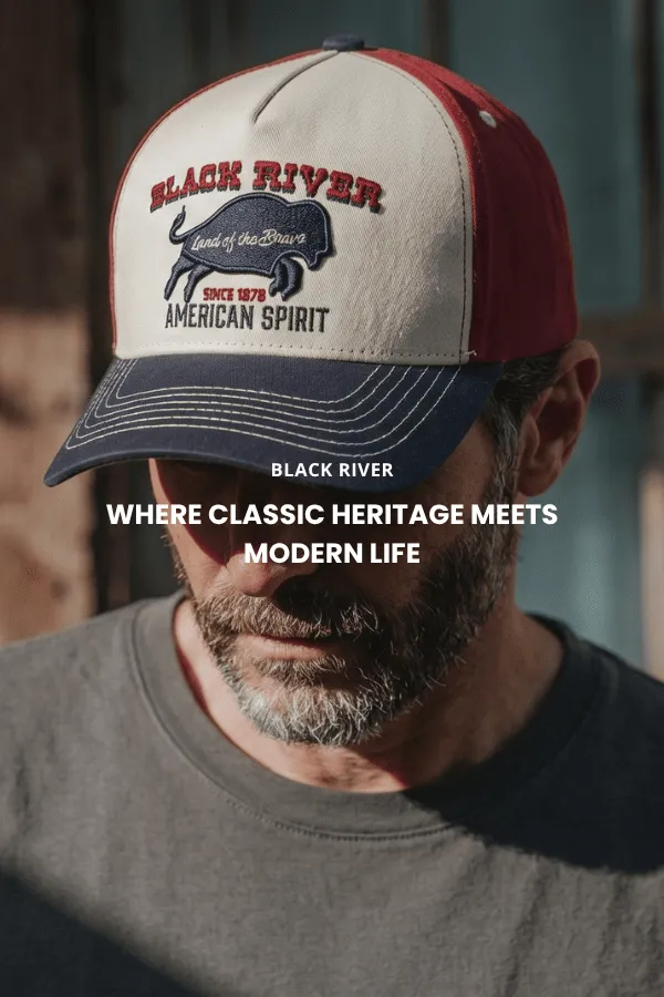 En mann sitter på en trekasse i et studio og bærer en klassisk brun cowboyhatt i filt med bred brem, en mørk denimskjorte og jeans.