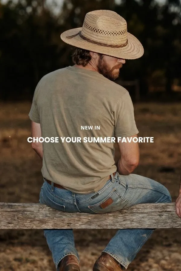 En mann sitter på en trekasse i et studio og bærer en klassisk brun cowboyhatt i filt med bred brem, en mørk denimskjorte og jeans.
